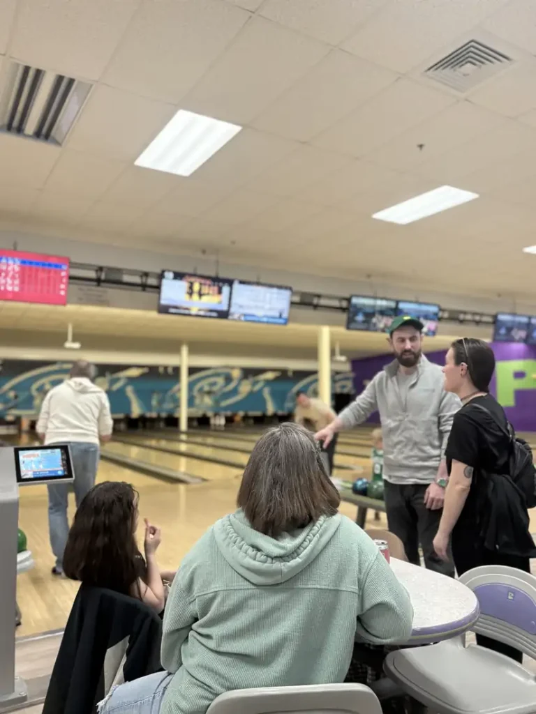 Attendees relaxing at tables beside the lanes at the Nashoba Springs bowling outing