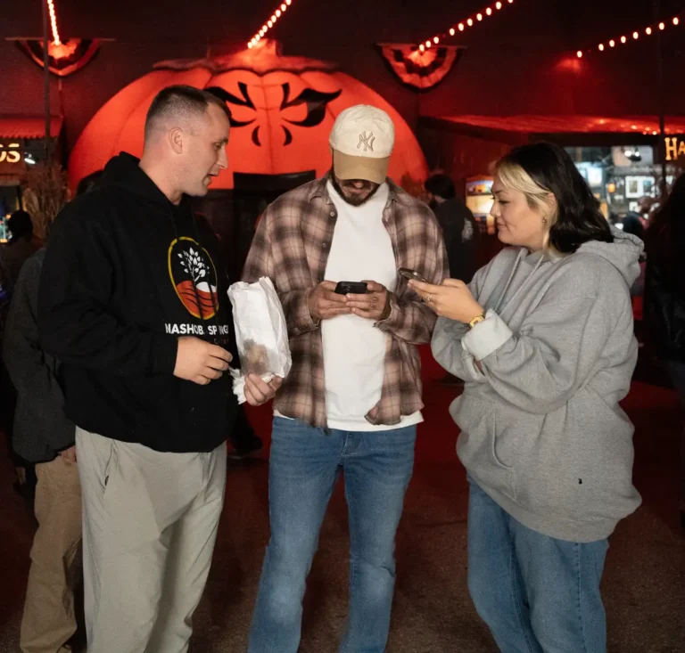 Three friends checking a phone under red lights at Fright Kingdom