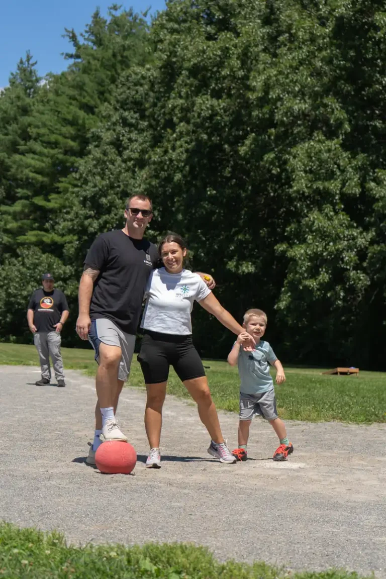 Adults and a child rolling the ball at the Nashoba Springs kickball outing